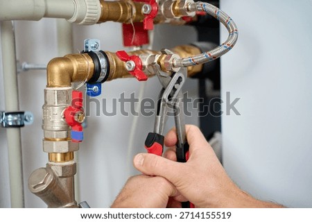 Close up of hands using adjustable wrench to tighten plumbing fitting with valves and flexible hose. Concept of plumbing installation, maintenance service and household engineering.
