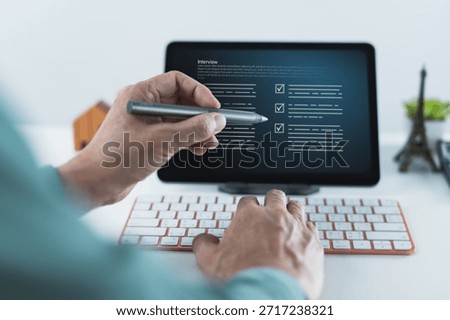 Close up of hands using a stylus and keyboard while reviewing a digital interview checklist displayed on a tablet screen in a clean workspace.