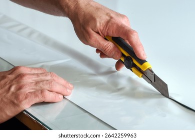 Close up of hands using utility knife cutting white vinyl adhesive film on glass table