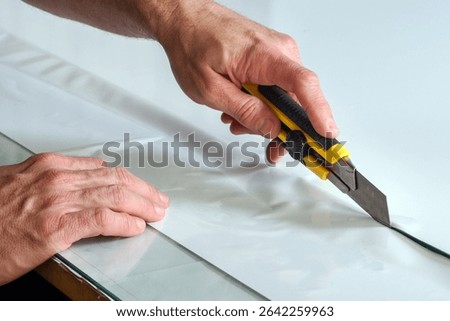 Close up of hands using utility knife cutting white vinyl adhesive film on glass table