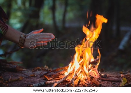 Close up hands warming over campfire concept photo. Make fire in forest. Side view photography with woman hands on background. High quality picture for wallpaper, travel blog, magazine, article