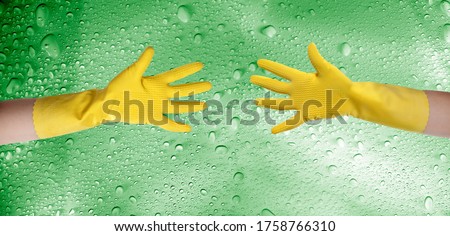 close up hands wearing yellow cleaning gloves over water drops covered background