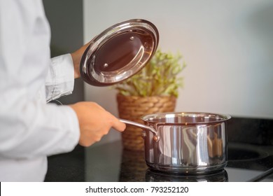 Close Up Hands Of Woman Holding Hot Pot Which Is On Electric Stove During Cooking Soup For Family In Kitchen. Homemade Cuisine For Healthy With Organic Vegetables. Cuisine Concept