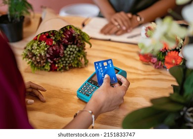 Close up of hands of woman paying bill with blue credit card by contactless to florist. Hands of woman customer make payment with credit card with NFC technology on terminal device.