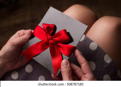 Close up of the hands of a woman with polka dress holding a black card with red ribbon above knees - Powered by Shutterstock