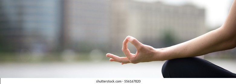 Close up of hands woman sitting in yoga Easy Sukhasana Pose on riverbank in the city, meditating with fingers in Jnana mudra. Horizontal photo banner for website header design with copy space for text