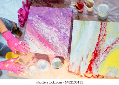 Close Up Of Hands Women Painter Finishing Creating Fluid Acrylic Abstract Painting In Art Class, With A Mess On The Table Full Of Bottle, Jars With Defferent Paint Colors. Art, Design Concept.