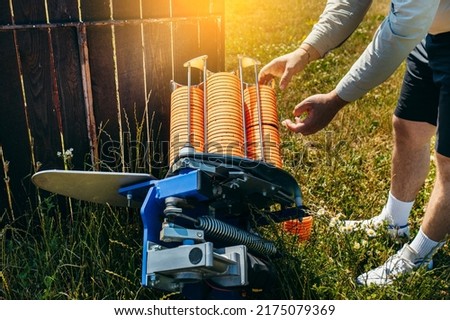 Close up hands of worker loading plat machine with orange shooting plate for shooting-ground training on field with grass