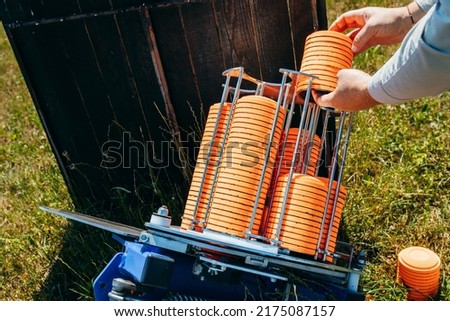 Close up hands of worker loading plat machine with orange shooting plate for shooting-ground training on field with grass