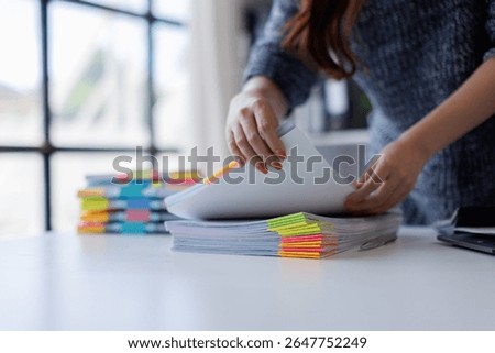 Close up of hands working in Stacks of paper files for searching and checking unfinished document achieves on folders papers on desk.

