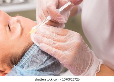 Close up of hands of young cosmetologist injecting in female face