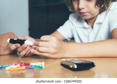 Close Up Of The Hands Of A Young Diabetic Patient Is Using A Lancing Device To Make A Blood Sugar Test On A Doctor Desk In His Office. Child Diabetes Concept