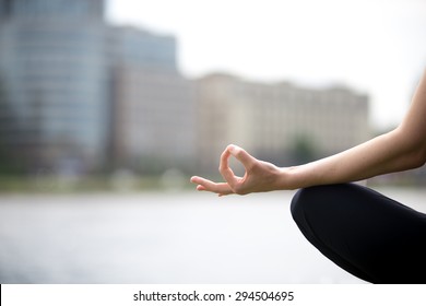 Close up of hands of young office yogi woman sitting cross legged in yoga Easy Sukhasana Pose on riverbank in the city, meditating with fingers in Jnana mudra