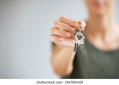 Close up of hands of young woman holding house keys of her new house. Woman hand holding housekey shaped keychain. Girl buying new home for her family and showing key with copy space.
