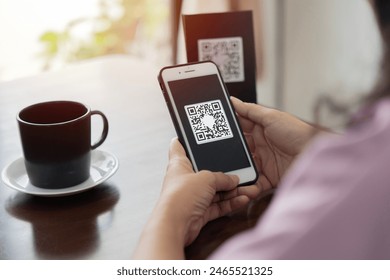 Close up of hands of young woman scanning qr code for cashless payment at cafeteria. Selective focus.