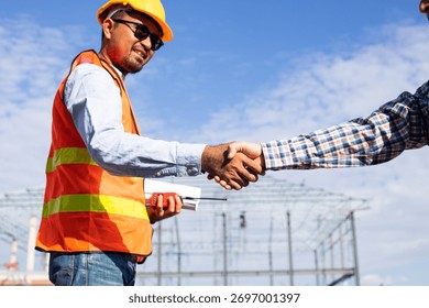 Close up handshake of two engineers on produce site. Group of industries workers meet on manufacture site shake hands