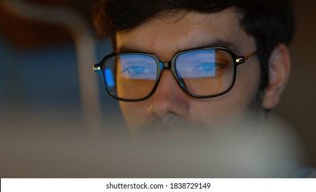 Close up of Handsome Businessman wearing glasses looking at pc screen using a desktop computer working at night in the office. Business Graph and chart reflection in his eyeglasses. Overworked Concept