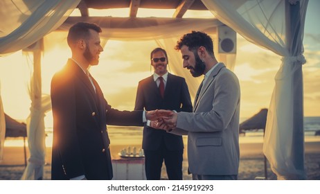 Close Up Of Handsome Gay Couple Exchange Rings And Kiss At Outdoors Wedding Ceremony Venue Near The Sea. Two Happy Men In Love Share Their Vows And Get Married. LGBTQ Relationship Goals.