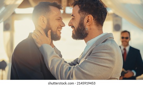 Close Up Of Handsome Gay Couple Exchange Rings And Kiss At Outdoors Wedding Ceremony Venue Near The Sea. Two Happy Men In Love Share Their Vows And Get Married. LGBTQ Relationship Goals.