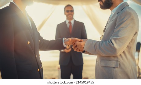 Close Up Of Handsome Gay Couple Exchange Rings And Kiss At Outdoors Wedding Ceremony Venue Near The Sea. Two Happy Men In Love Share Their Vows And Get Married. LGBTQ Relationship Goals.