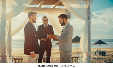 Close Up Of Handsome Gay Couple Exchange Rings And Kiss At Outdoors Wedding Ceremony Venue Near The Sea. Two Happy Men In Love Share Their Vows And Get Married. LGBTQ Relationship Goals.