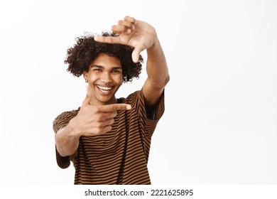 Close Up Of Handsome Guy Looking Through Hand Camera Frame And Smiling, Imaging Smth, Searching Right Angle, Stands Over White Background