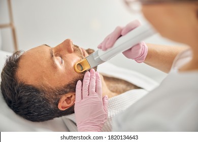 Close up of handsome young man with closed eyes having laser hair removal procedure in beauty salon