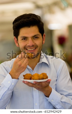 Close up of a handsome young man eating a homemade fritters with sugar and its ingredients