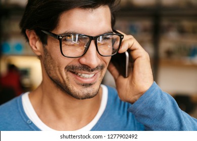 Close Up Of A Handsome Young Man Wearing Glasses At The Library, Talking On Mobile Phone