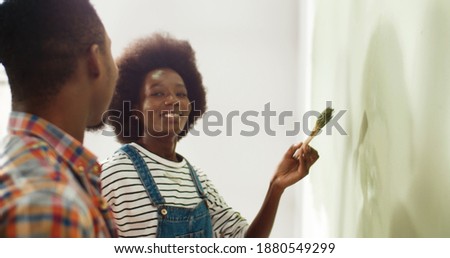 Close up of happu married young African American wife and husband painting walls in apartment with paintbrushes and having fun, laughing and painting on each other's faces. Home repair concept