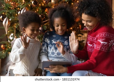 Close up happy African American family making video call to relatives on Christmas, sitting near festive tree at home, smiling mother with two kids using tablet, chatting online, waving hands - Powered by Shutterstock