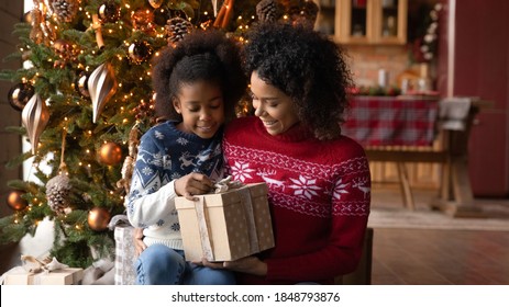 Close Up Happy African American Woman With Adorable Daughter Opening Christmas Gift Box, Sitting On Floor Near Festive Tree At Home, Smiling Mother And Little Girl Hugging, Unpacking Present