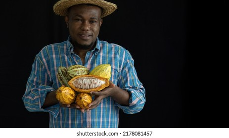 Close Up Happy African Man Or Farmer Holding Cacao Or Cocoa Fruits In Arms, Looking At Camera On Black Background With Copy Space.