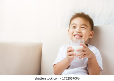 Close Up Of Happy Asian Little Cute Kid Or Child Boy Hand Holding Milk Glass He Drinking White Milk During Sitting On The Sofa At Home After Lunch. Daily Life Health Care Medicine Food