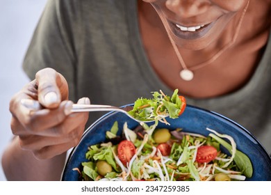 Close up of happy black woman eating healthy salad with green fresh ingredients. Smiling vegetarian woman holds bowl of fresh salad while eating tomatoes and carrot with fork. 