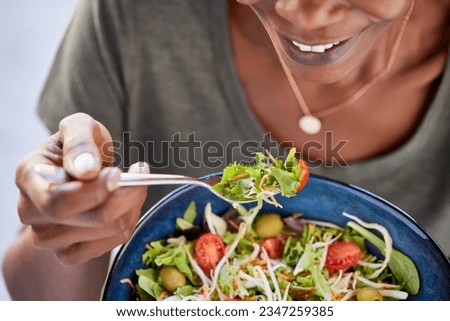 Close up of happy black woman eating healthy salad with green fresh ingredients. Smiling vegetarian woman holds bowl of fresh salad while eating tomatoes and carrot with fork. 