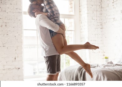 Close up of happy boyfriend holding beloved girlfriend in arms, romantic millennial couple hugging kissing in bedroom, man lifting up lover enjoying passionate dance at home, spouses relax swirling