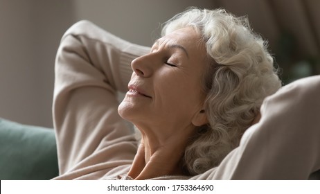 Close up of happy calm elderly female relax on comfortable sofa at home sleeping or taking nap, smiling peaceful mature woman rest on couch, breathe fresh air or meditate, stress free, peace concept