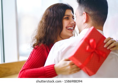 Close up of happy couple with christmas gift hugging. Cheerful couple with gift in hands enjoying together on Christmas eve. Lovers give each other gifts. Valentine's Day concept. - Shutterstock ID 1586988394
