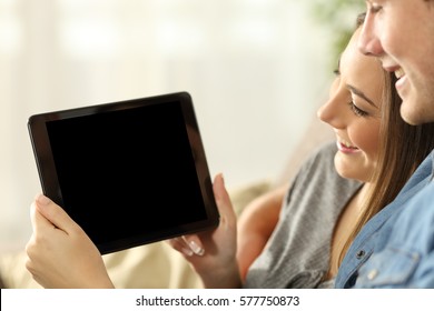 Close up of a happy couple watching media in a tablet and showing the blank screen sitting on a sofa in the living room at home - Powered by Shutterstock