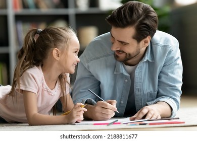 Close up happy father   adorable daughter drawing and pencils  young dad   little girl lying warm floor and underfloor heating  family enjoying creative activity  leisure time at home