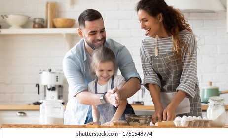 Close up happy father clapping hands with flour hugging daughter near mother looking at husband in kitchen at home. Smiling couple with child playfully cooking dinner with baking pastry. - Shutterstock ID 1761548774