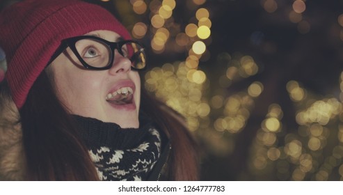 Close Up Of The Happy Girl Looking Charmed At Something On The Blurred Christmas Lights In The Night. Portrait Shot. Outside