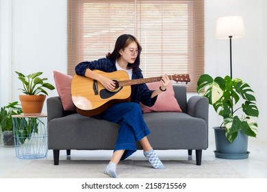 Close up happy glasses Asian girl playing acoustic guitar in living room at home. Recreation at home concept.