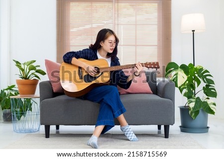 Close up happy glasses Asian girl playing acoustic guitar in living room at home. Recreation at home concept.