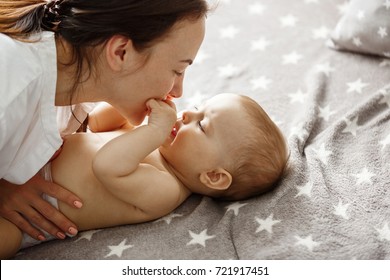 Close up of happy good looking mother playing with her newborn son, kissing and gently biting his little hands. Happy motherhood concept. - Powered by Shutterstock