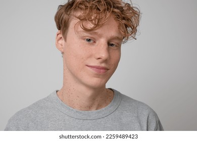 Close up of happy handsome freckled red haired smiling teenager with blue eyes wearing gray t-shirt casual wear showing emotions and looking at the camera posing for photo against the gray backdrop.  - Powered by Shutterstock