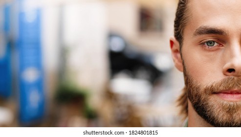 Close Up Of Happy Handsome Man Looking At Camera While Standing Outdoors On Blurred Background. Half Face Of Caucasian Bearded Guy With Smile On Face.