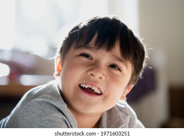 Close Up Happy Kid Looking Up With Smiling Face, High Key Light Healthy Child Relaxing At Home, Positive Little Boy Having Fun On His Own In Living Room With Blurry Sunny Light Background.