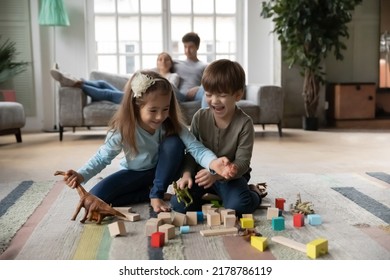 Close up happy kids cute sister and brother playing with colorful toys together while parents relaxing on couch, laughing happy little girl and boy sitting on warm floor with underfloor heating - Powered by Shutterstock